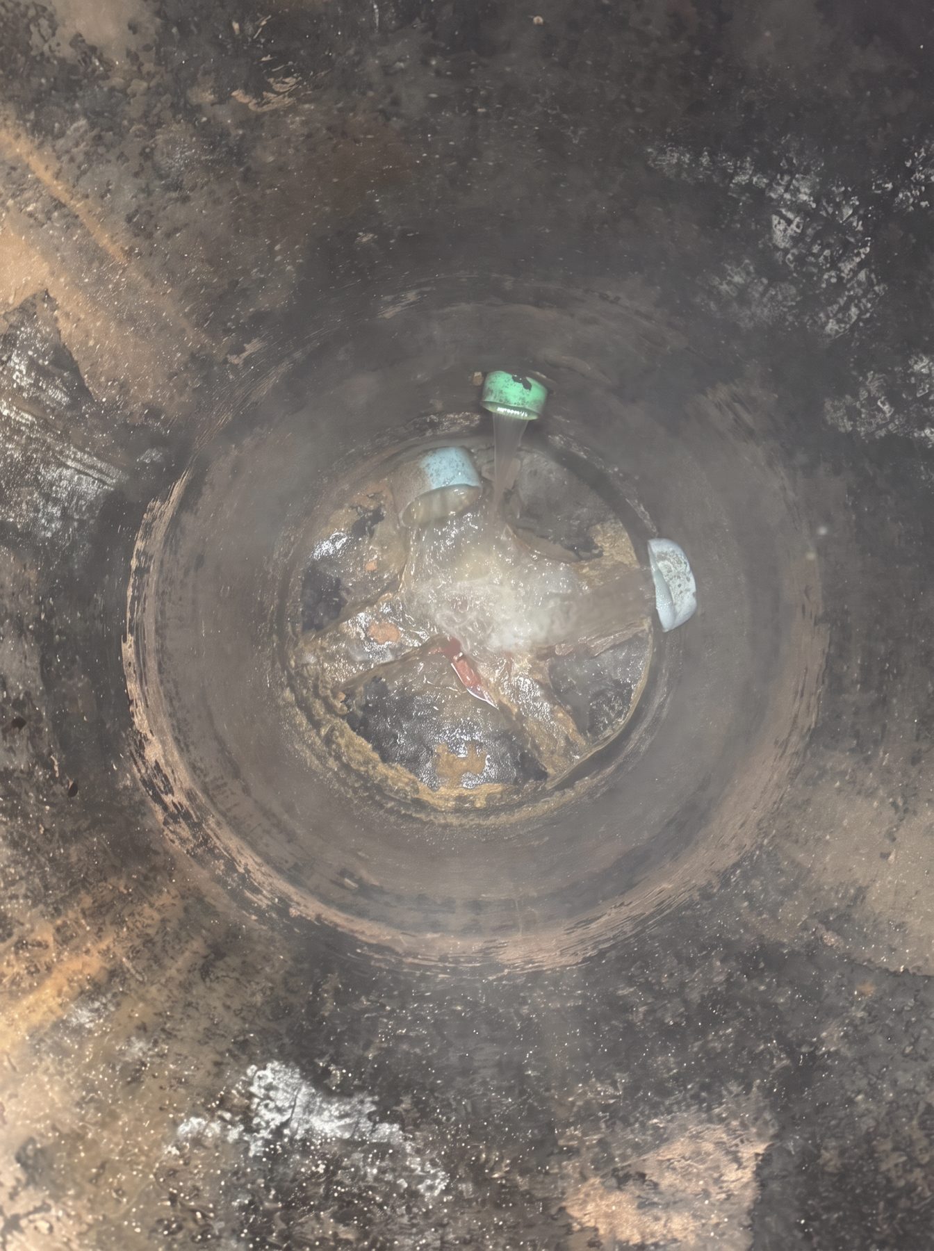 Deteriorated sanitary manhole invert showing severe H2S corrosion, pitted walls, and eroded bench prior to CEI rehabilitation