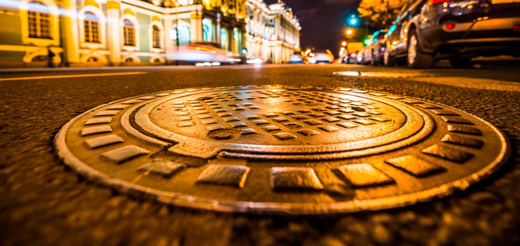 Illuminated manhole cover on a downtown street at night — the infrastructure CEI rehabilitates from below